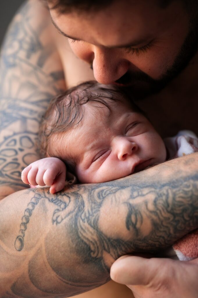 photo d'une bébé dans les bras de son papa tatoué lors d'une séance photo nouveau-né à domicile à narbonne par LONOWAÏ Photographie