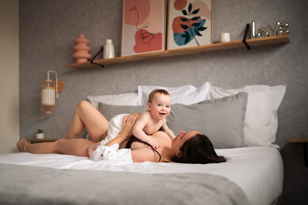 photo d'une femme peu vêtue allongée dur le dos sur un lit qui caline son bébé en peau à peau. photo prise lors d'une séance de maternité intimiste à Narbonne par LONOWAÏ Photographie