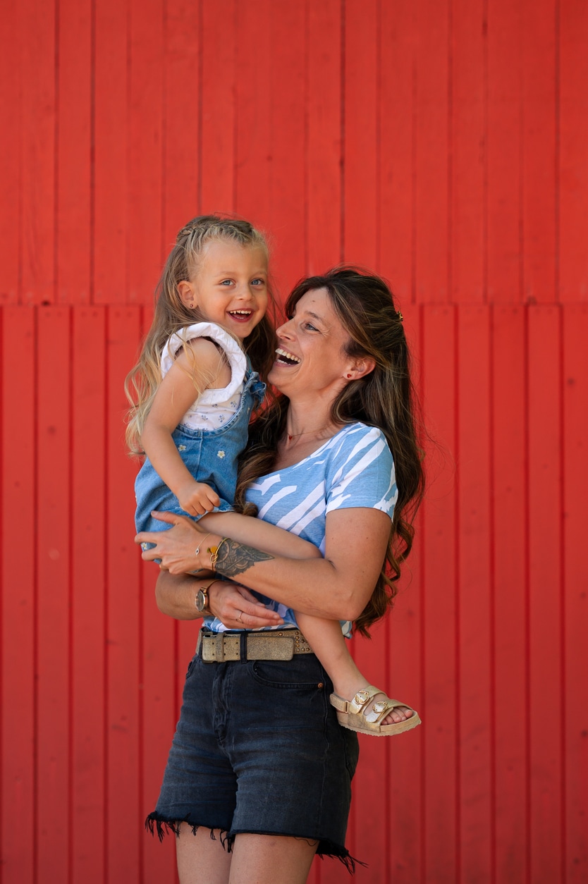 photo d'une mère avec sa fille lors d'une séance famille. Rires devant une porte rouge, complicité. Narbonne LONOWAÏ Photographie