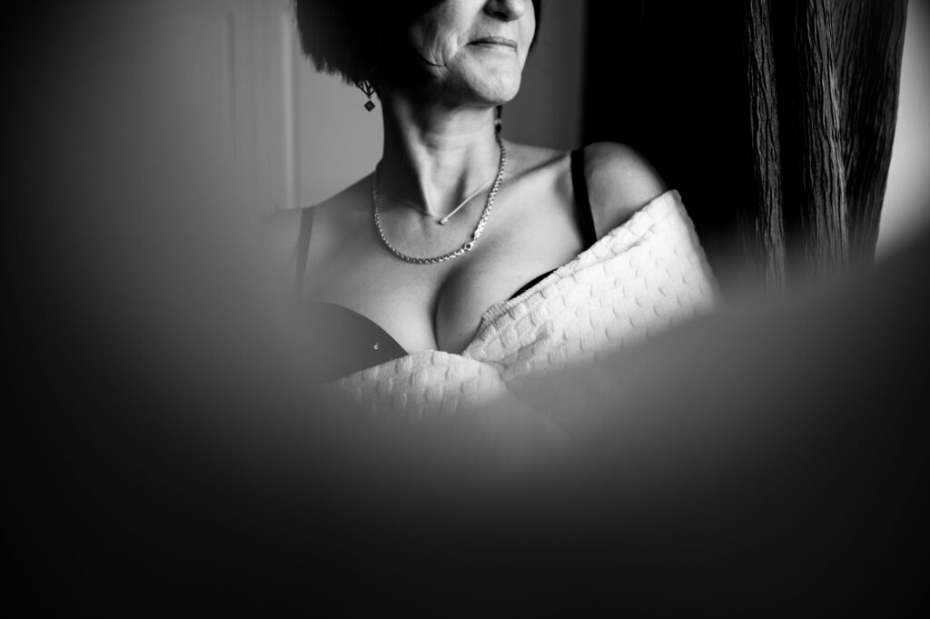 photo d'une femme au décoltté plongeant vue à travers un rideau, sourire au lèvre. séance photo boudoir, séance photo intimiste femme à narbonne par LONOWAÏ Photographie