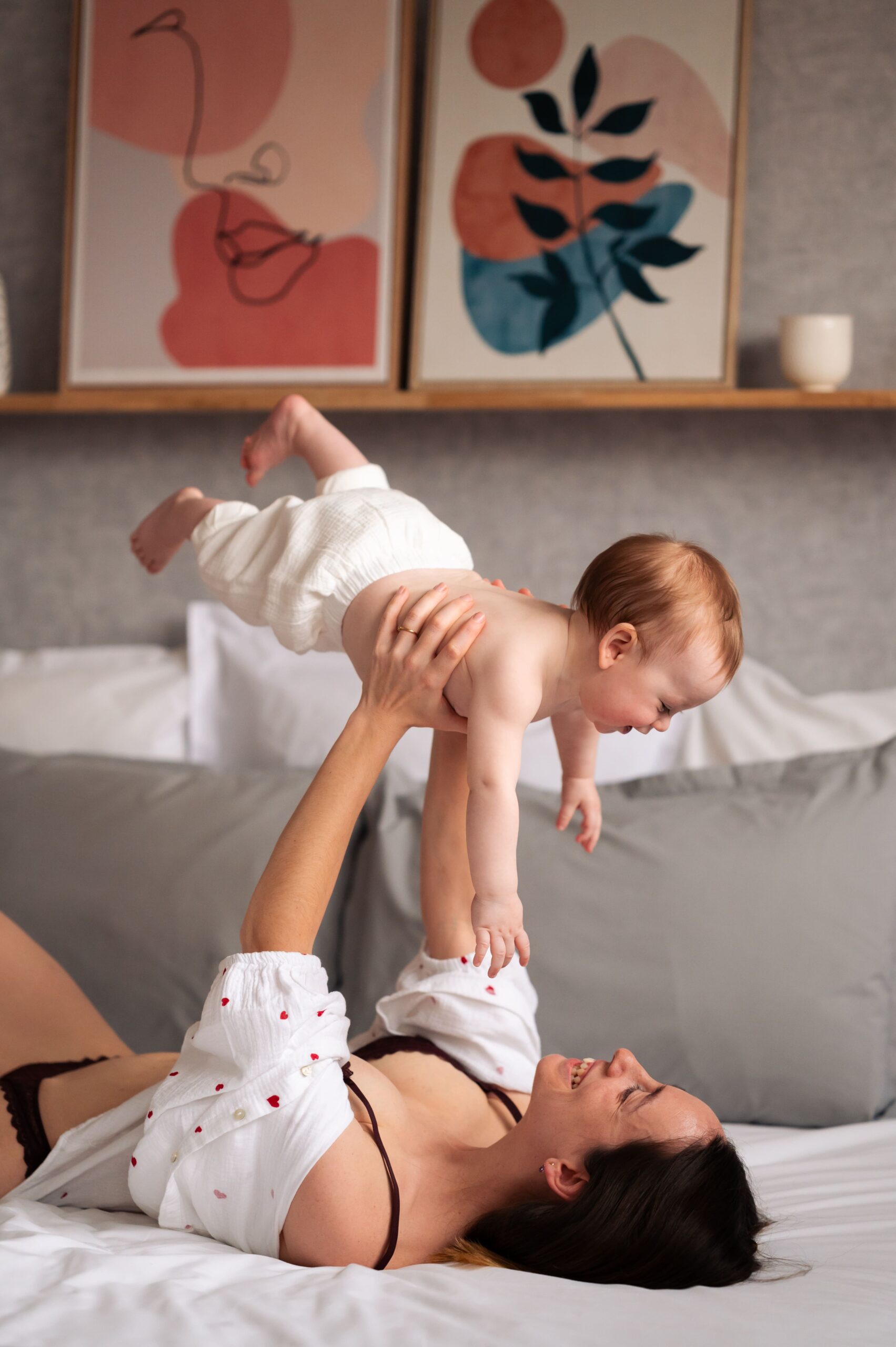 femme allongée sur un lit qui tient son bébé en l'air. Mmoment de complicité lors d'une séance de maternité intimiste à Narbonne par LONOWAÏ Photographie