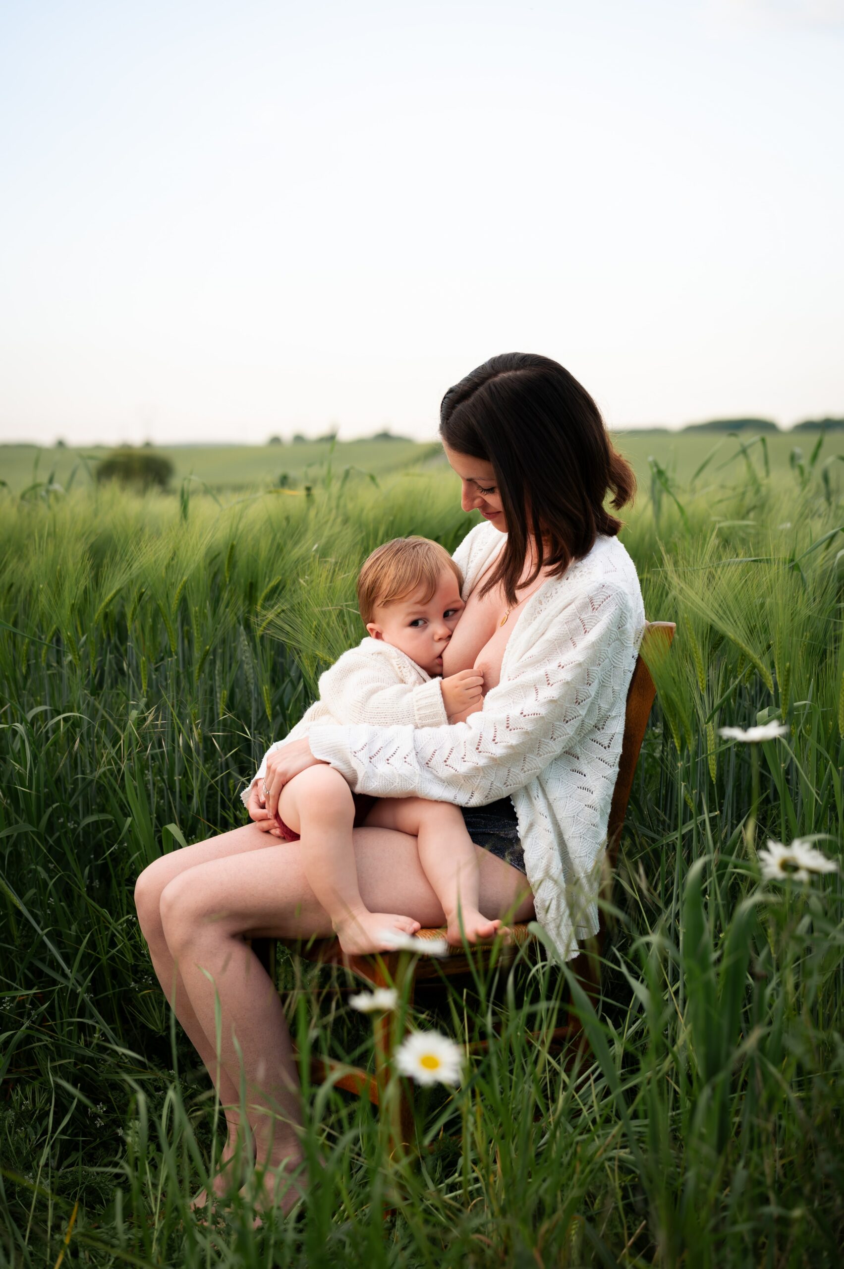 femme assise sur une chaise dans un champ. Elle allaite son bébé de 18 mois. Photo prise lors d'une séance de maternité intimiste par LONOWAÏ Photographie à Narbonne